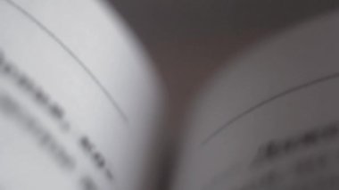 Hardcover kitabının sayfalarında siyah harflerle yazılmış kelimelerden oluşan yazılı metin satırları, beyaz kağıttan yapılmış sayfalar üzerinde kameranın yukarıdan aşağıya hızlı hareketi ve değişken odaklı yakın odaklı.