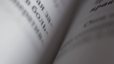 Beyaz kağıttan yapılmış bir kitabın sayfalarında siyah harflerle yazılmış kelimelerden oluşan yazılı metin satırları, ders kitabının katları, kameranın aşağıdan yukarıya, değişken odaklı hareketi