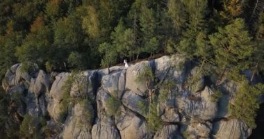 Gün batımında beyaz elbiseli bir çift, sarı ve yeşil sonbahar ağaçlarıyla dağlardaki büyük kayaların üzerinde öpüşüyor. Quadcopter hızla gökyüzüne yükselir ve dağın tepesinde çayırlar vardır.