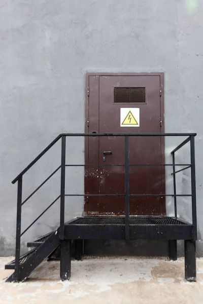 Kahverengi kapıdaki yüksek voltaj tabelası. Tehlike bölgesi. Elektrik var. Şehirdeki işaretler.