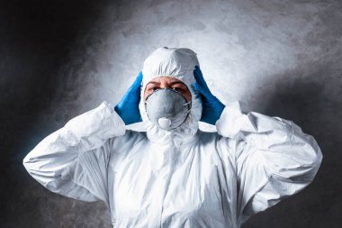 Viral koruyucu giysili beyaz maskeli virüs uzmanı başını tutuyor kameraya korkuyla bakıyor ve koronavirüs salgınını nasıl durduracağını ve ne yapacağını düşünüyor. Bu işin tehlikelerini düşünüyor..