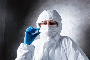 Tıbbi maskeli bir hemşire ve viral koruyucu giysi. Doktor, tıbbi maske ve viral koruyucu giysiyle masada oturuyor. Doktor elinde bir hap tutuyor..