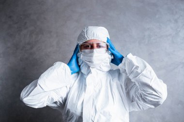 Viral koruyucu giysili beyaz maskeli virüs uzmanı başını tutuyor kameraya korkuyla bakıyor ve koronavirüs salgınını nasıl durduracağını ve ne yapacağını düşünüyor. Bu işin tehlikelerini düşünüyor..