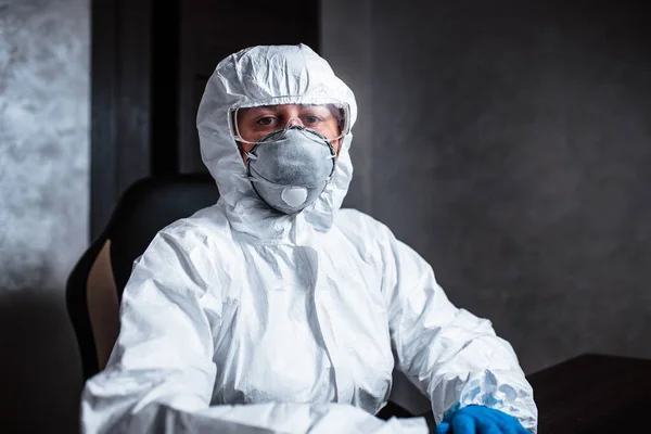 A nurse in a medical face mask and viral protective suit. The doctor is sitting at the table in a medical face mask and a viral protective suit.