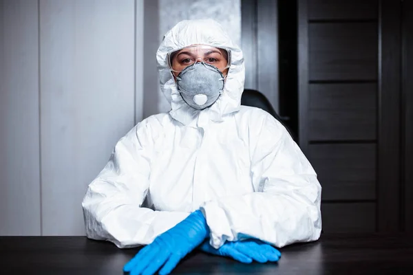 A nurse in a medical face mask and viral protective suit . The doctor is sitting at the table in a medical face mask and a viral protective suit.