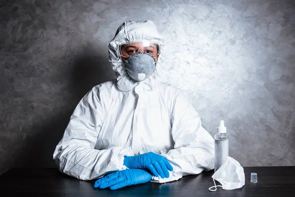 Nurse in a medical face mask and a viral protective suit. The doctor is sitting at the table in a medical face mask and a viral protective suit. The doctor is sitting next to pills and antiseptic.