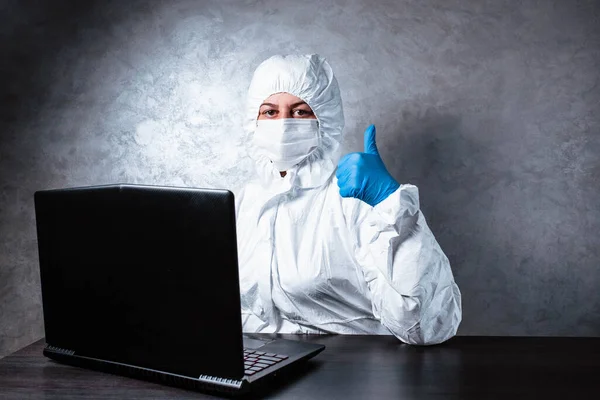 Beyaz maskeli ve tıbbi eldivenli bir virüs uzmanı, beyaz koruyucu bir takım elbise giyiyor, dizüstü bilgisayarla çalışıyor ve sınıfı eliyle gösteriyor. Salgın yüzünden izole edilmiş ve paniklemiş..