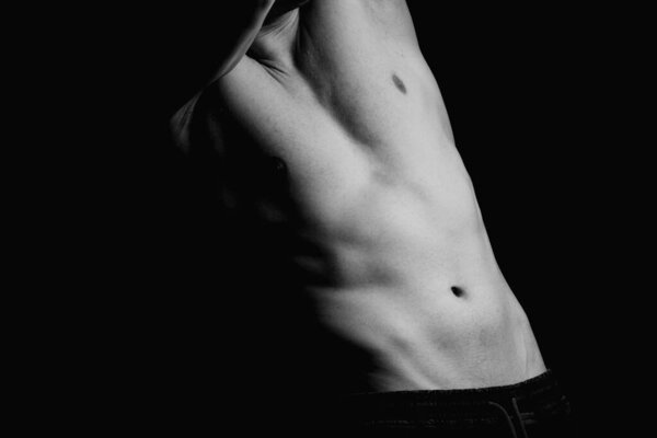 Сильный спортсмен, бодибилдер. Неузнаваемый, без портрета. Голый торс, мускулистое тело. Сильные грудные и плечевые мышцы. Студийная съемка на черном фоне, низкий ключ. Концепция культуризма
