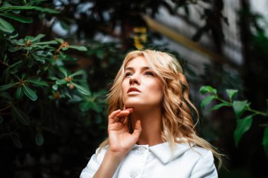 Yeşillik arka planında gelinlik giymiş çekici sarışın bir gelinin portresi. Botanik yeşili bahçesindeki gelin. Kıvırcık sarı saçlı güzel bir genç kadın. Evlilik..