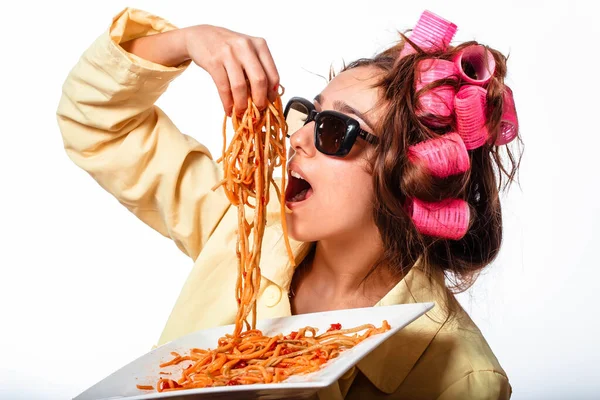 Kıvırcık elbiseli kız, makarna ve çatallı tabak ketçaplı makarna yiyor ve beyaz arka planda gözlüklü duruyor. Spagetti yiyen kız. Elinde bir tabak makarna tutan kız..