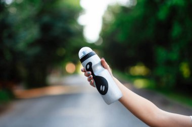 Spor yaptıktan sonra su içen ya da dışarıda koşan genç bir kadının portresi. Kız egzersiz sırasında vücut sıvısına önem verir. Susamış kadın su şişesini tutuyor. Susuzluk ve su dengesi kavramı.