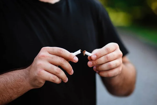 World No Smoking Day. The fight against nicotine addiction. The guy breaks a cigarette. Male hand crushing cigarette. Concept Quitting smoking, World No Tobacco Day. No Smoking.