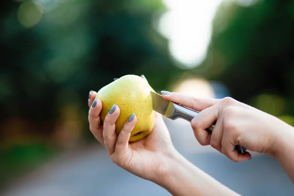 Female hands with a knife cut out a core from an apple - cooking close up. The girl cuts an apple with a knife. Person cuts a green apple with knife.