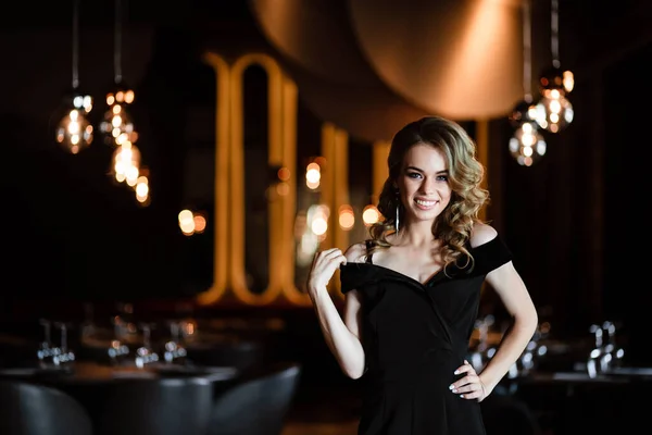 Beautiful blonde, young girl. Portrait of a young girl in a restaurant. Young girl in a restaurant on a black background. Portrait of a girl in a black dress. Young girl.