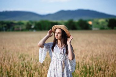Buğday tarlasında bir kızın portresi. Buğday tarlasında beyaz elbiseli ve şapkalı güzel bir kızın portresi. Beyaz elbiseli ve şapkalı kız. Buğday tarlası. Doğada genç bir kadının portresi..