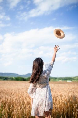 Buğday tarlasında arkadan bir kızın portresi. Buğday tarlasında beyaz elbiseli ve şapkalı güzel bir kızın portresi. Beyaz elbiseli ve şapkalı kız. Buğday tarlası.