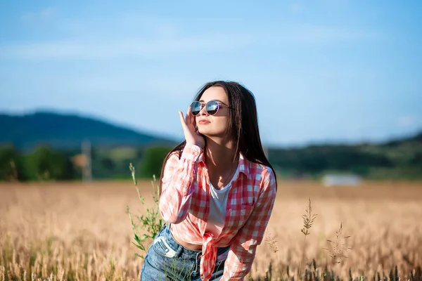 Buğday tarlasında bir kızın portresi. Buğday tarlasında gözlüklü ve gömlekli bir kız. Buğday tarlasında gömlek ve güneş gözlüğü takmış güzel bir kızın portresi. Gözlük ve güneş gözlüğü. Buğday tarlası.