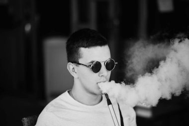 Genç yakışıklı adam tek başına nargile içiyor. Genç adam nargile içiyor. Nargile ve kömürden kıvılcımlar. Shisha, kıvılcım, nargile kıvılcımı. Genç adam güzel kokulu doğu nargilesi içiyor..