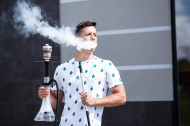 Genç yakışıklı adam tek başına nargile içiyor. Genç adam nargile içiyor. Nargile ve kömürden kıvılcımlar. Shisha, kıvılcım, nargile kıvılcımı. Genç adam güzel kokulu doğu nargilesi içiyor..