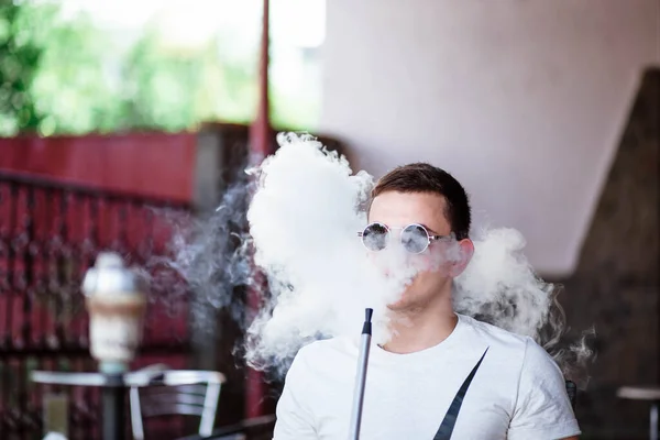 Genç yakışıklı adam tek başına nargile içiyor. Genç adam nargile içiyor. Nargile ve kömürden kıvılcımlar. Shisha, kıvılcım, nargile kıvılcımı. Genç adam güzel kokulu doğu nargilesi içiyor..