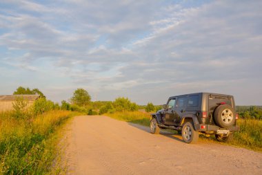 Leningrad region, Rusya Federasyonu, 27 Temmuz 2018: Jeep Wrangler akşam güneşin kırsal bir yolda. Wrangler kompakt dört tekerlekli arabayla yol ve spor yeni araç kapalı olduğunu
