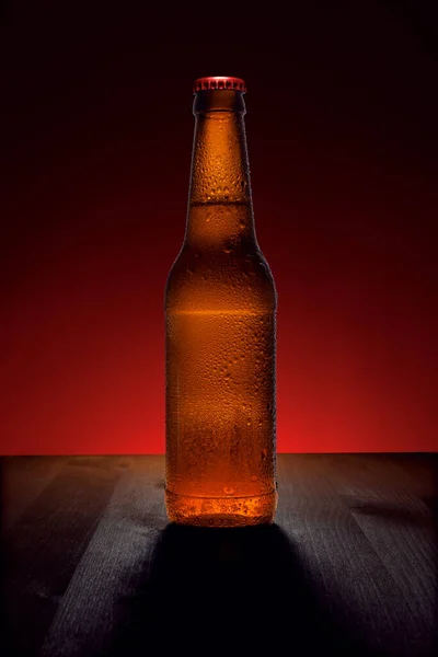 Cerveza en una botella sobre una mesa de madera con un fondo retroiluminado. Bebida fría en una botella . — Foto de Stock