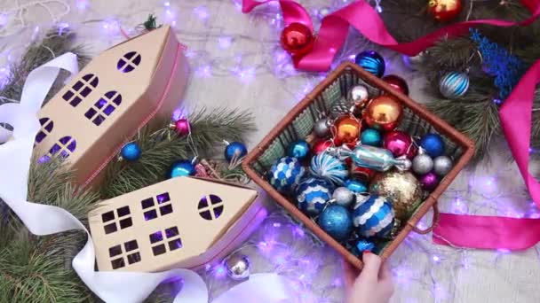 Руки женщины держат коробку с рождественскими игрушками на фоне ветвей елки и шагов гаргоев. Вид сверху — стоковое видео