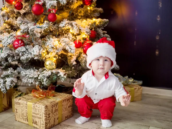 Çocuk 1 yaşında evde zarif bir Noel ağacı altında kırmızı Santa şapka içinde — Stok fotoğraf