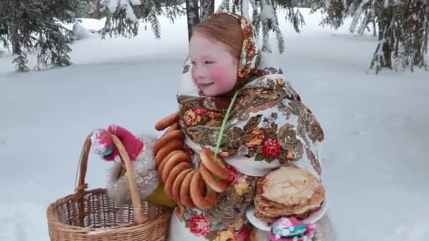 Όμορφη κοκκινομάλλα ρωσική κορίτσι με ένα μαντήλι στο δρόμο με ένα ψάθινο καλάθι με τα χέρια και τηγανίτες. Ρωσική διακοπών Maslenitsa — Αρχείο Βίντεο