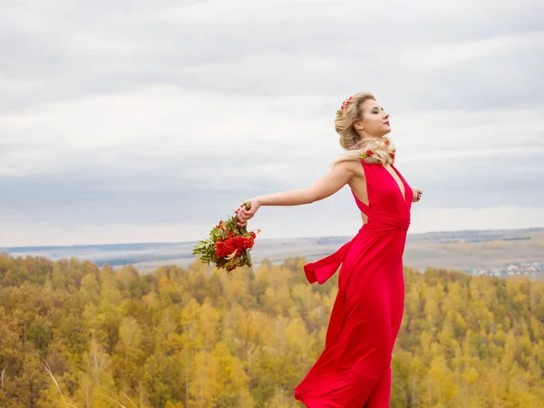 Krásná dívka v dlouhé červené šaty s rowan kytice na podzim — Stock fotografie