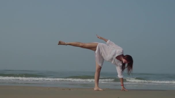 Молода жінка практикує йогу на пляжі в морі. Фітнес, спорт, йога та здоровий спосіб життя. 4-кілометровий — стокове відео