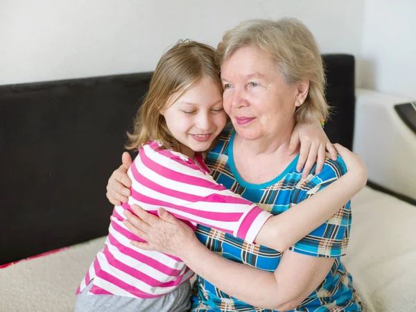 Happy grandmother and granddaughter hugging at home on the couch