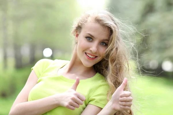 Beautiful white girl shows thumb up on nature in the park — Stock Photo, Image