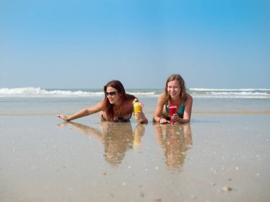 Bir bardak meyve suyu ellerinde iki beyaz kızla sahilde kum yalan söylüyorsun