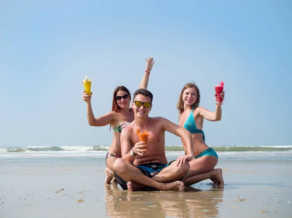 Två tjejer och en man på stranden dricka saft från glas glasögon — Stockfoto