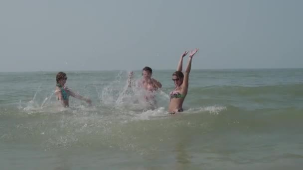 Una compañía de jóvenes alegres se bañan en olas del mar con salpicaduras en un día caluroso. 4K — Vídeo de stock