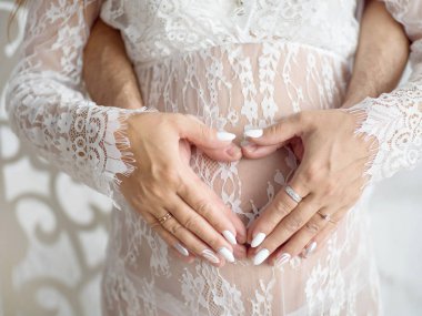 Beyaz peignoir hamile kız, bir kalp şeklinde karın kadın ve erkek elleri, closeup