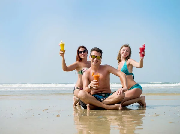 Ett sällskap av unga människor koppla av på stranden med saft i sina händer — Stockfoto