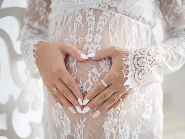 Manos femeninas en forma de corazón en el vientre de una mujer embarazada — Foto de Stock