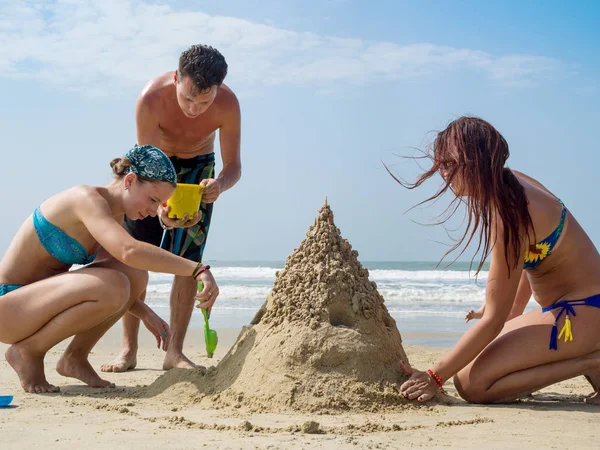 Ett ungt sällskap av människor bygger ett sandslott på stranden — Stockfoto