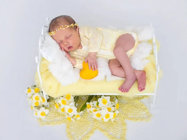 A little newborn baby with a yellow decorative heart in her hands is sleeping in the bed. — Stock Photo, Image