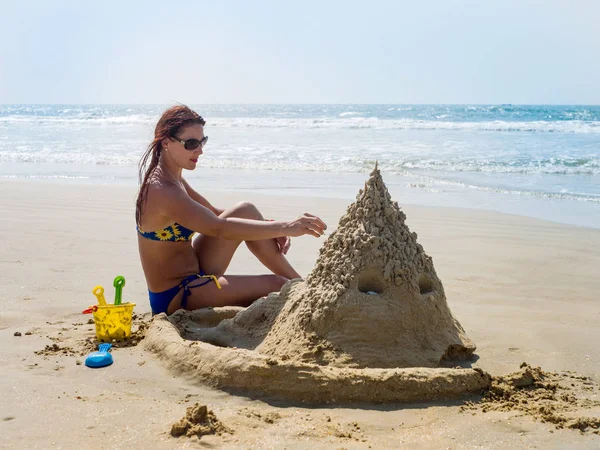 Het meisje op het strand bouwt een zandkasteel. — Stockfoto