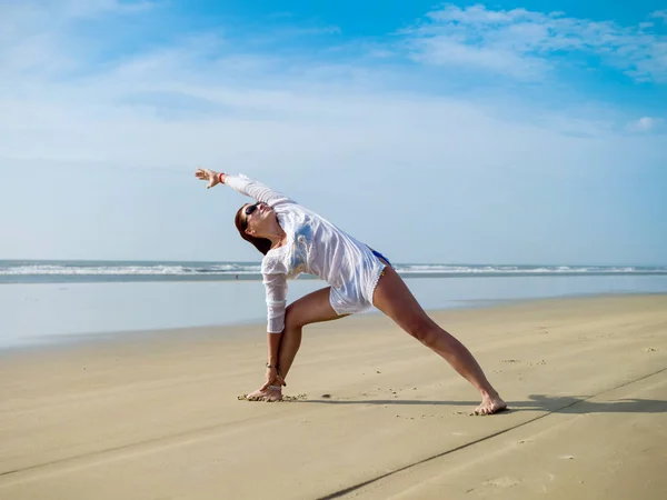 Young woman in white tunic doing yoga by the sea — Stock Photo, Image