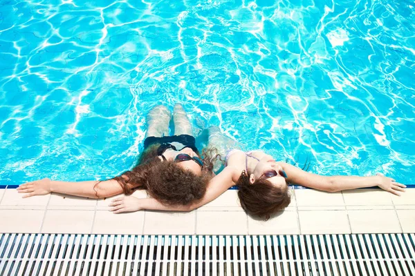 Dos hermosas chicas en gafas de sol disfrutando de la piscina —  Fotos de Stock