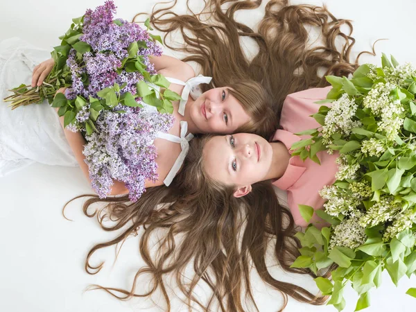Portrét krásných šťastných sestřiček s dlouhými vlnitými vlasy a kyticí lilacami — Stock fotografie