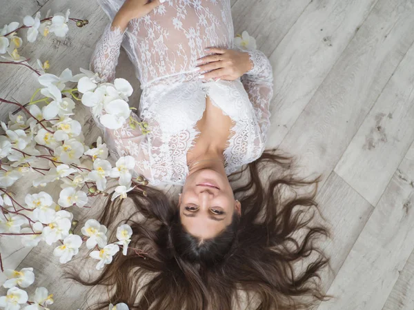 Krásná těhotná žena v bílých šatech má ruce na břiše ležící na podlaze — Stock fotografie