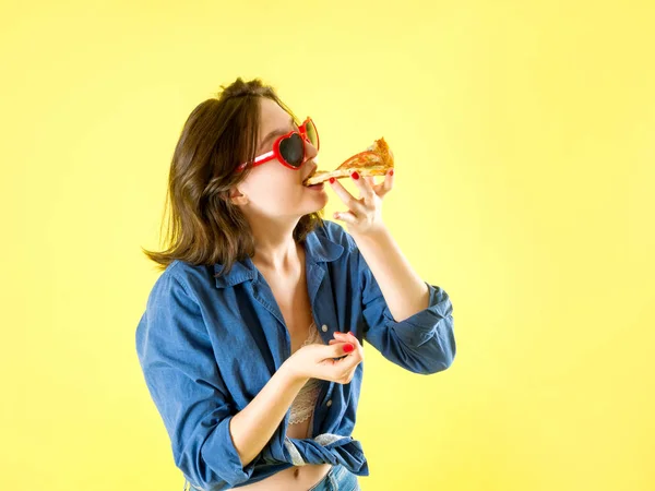Молода дівчина їсть піцу на жовтому тлі. Реклама піци — стокове фото
