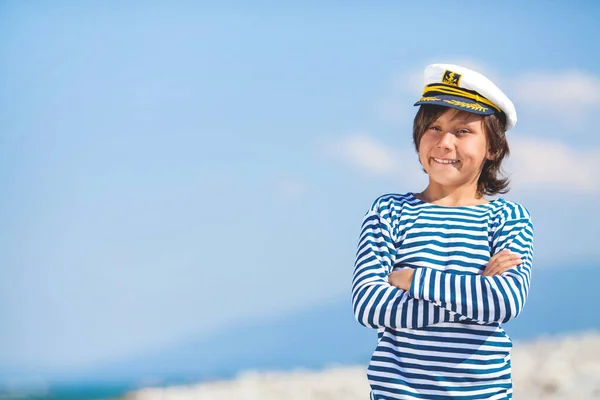 Little smiling captain boy looks into the distance on a blue sky background with place for text — Stock Photo, Image