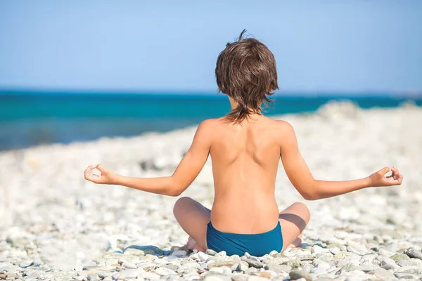 The boy sits with his back on the seashore in the lotus position. Meditation. — Stock Photo, Image