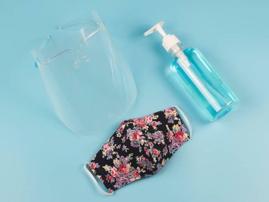 Coronavirus veya COVID-19 önleme ve yeni normal yaşam tarzı kavramı. Yüzün üst görünüşü, alkol el dezenfektanı jeli ve çiçek desenli maske mavi arka planda..